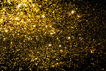 Golden bokeh background. Golden glitter on a black background.Festive New Year and Christmas shiny glitter layout.