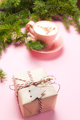 Side view of gift box and cup of latte with art in shape of Christmas tree on pink background with branch of fir tree. Copy space for your text