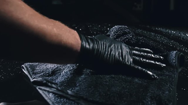 Using rag in palm of your hand, drops are removed from the car. Drop flow down the hood. Close up view of bonnet car. Process of polishing and washing auto. Hose is poured over cowl with water.