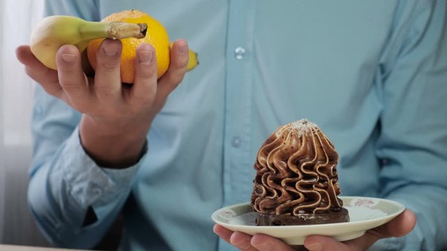 A man shows fruit and a cake in his hands. Choosing a healthy diet and fruit diet. slimming and healthy eating concept