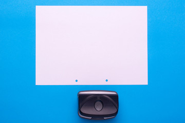Hole punch and a sheet of white paper. View from above. Free space for an inscription.