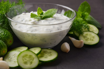 Fresh cucumber and dill sauce Tzatziki and ingredients on dark background.