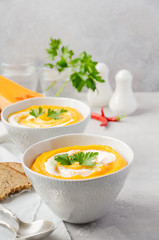 Pumpkin soup with cream and parsley on a gray concrete or stone background.