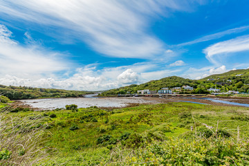 Fototapeta na wymiar Clifden harbor at low tide seen from a hill, surrounded by trees and green vegetation, sunny spring day with a blue sky and white clouds in the province of Connacht, Ireland