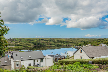 Fototapeta na wymiar Clifden Bay surrounded by green vegetation seen from a hill with houses, mirror reflection in the water, spring day with a blue sky and abundant clouds in the Connacht province, Ireland