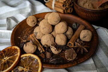 Handmade chocolate truffles on vintage clay plate with fragrant spices on dark background