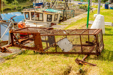 Obraz premium Old and rusty empty fishing trap, for lobsters or crabs next to a fishing boat on the pier of the port of Clifden, sunny spring day in the province of Connacht, Ireland