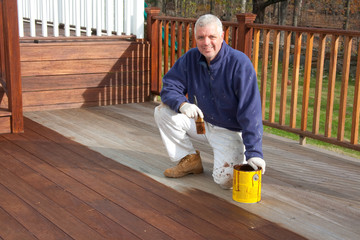 painter staining a deck in the spring