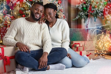Obraz premium Portrait of romantic black couple sitting on floor near Xmas tree