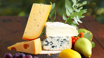 Camembert, brie, hard cheese and grapes on wooden stand. Pieces of different cheeses, pear and lemon on a blurred background. Dorblu and soft cheese on wooden boards. Widescreen