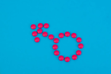 Pink pills laid out in the form of a male symbol. Shield and spear of Mars. On a blue background, copy space. Medicine for men.