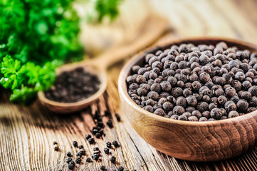 Black pepper. Pile of black pepper in wooden bowl. Wood spoon. full of pepper in background with green leaf.