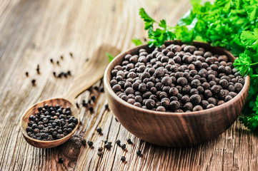 Black pepper. Pile of black pepper in wooden bowl. Wood spoon. full of pepper in background with...
