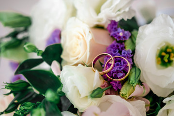 gold wedding rings close-up on a background of a bouquet of white roses and eustomas with green leaves