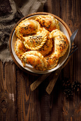 Baked dumplings (pierogi) with mushroom stuffing in a ceramic bowl on a wooden table, top view. Vegetarian dish