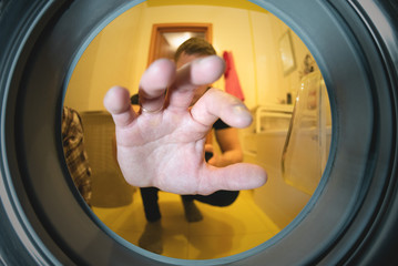 Man hand put dirty clothes in washing machine. View from a drum of washer. Laundry concept.