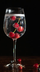 Gin and cherry cocktail in a glass with red fruits floating taken in studio with a dark background in portrait ratio