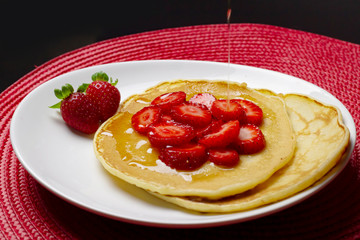 Putting syrup on top of pancake with  strawberries.