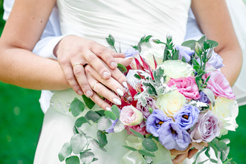 bride and groom hold hands, sunny day, hands with wedding rings close-up on a background of a bouquet of roses and eustomas