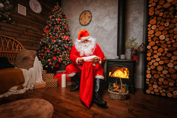 Santa Claus sits in a chair inside of his house and look into his opened bag with gifts for christmas greetings. Beautiful home decoration