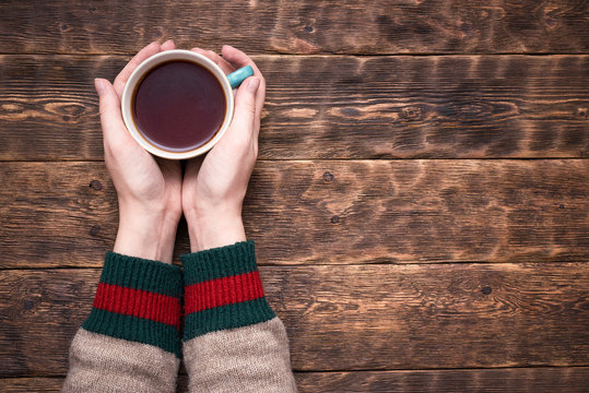 Female Hands In Sweater With A Cup Of Hot Tea Above Wooden Table Background With Copy Space.