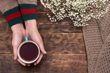 Fototapeta na wymiar Female hands in sweater with a cup of hot tea above wooden table background.