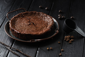 Homemade chocolate cake kladdkaka in vintage dish with coffee beans and vanilla pods on black background