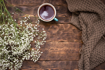 Hot tea, warm scarf and white flower on wooden table background.