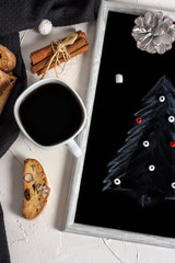 Winter Christmas composition. A cup of coffee on a table with Bisconti cookies, cinnamon and a black slate board with a Christmas tree pattern. Christmas mood concept. Layout concept. Top view