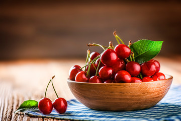 Cherries in wooden bowl with green leaf on top. Fine red cherry on table with copy space.