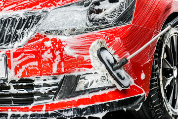 Car washing concept. Cleaning front lights using brush and foam. Selective detail focus..