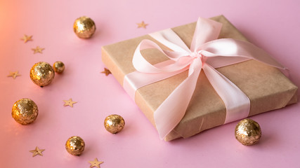 Gift in craft paper with a pink bow on a pink background with holographic sparkles in the form of stars and gold balls. Template  banner for greeting card your text design 2020. New year, christmas