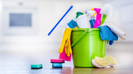 Basket or bucket with cleaning items on blurry modern kitchen background. Washing set colorful with...