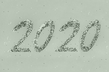 Golden sparkles shaped 2020 on background toned pale green color.