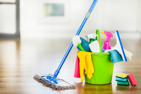 Bucket with cleaning items on blurry modern kitchen background. Washing brush and spray set with copy space.