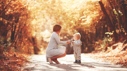 Young mother plays with her son in the autumn forest. Blond in a sports gray suit. Autumn leaves. Joyful family in nature