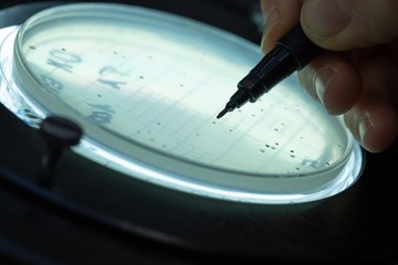 Man writes with felt-tip pen on a Petri dish under magnifying glass