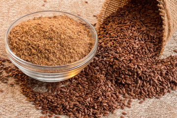 Flax seeds in linen cloth and miiled seeds in glass bowl on the  table.