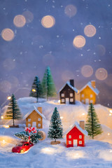Fototapeta premium Miniature wooden houses village on the snow over blurred Christmas decoration background, toned