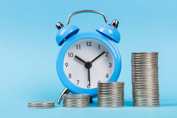 copy spaсe, stacked coins one on one in ascending order on the background of the alarm clock, blue background