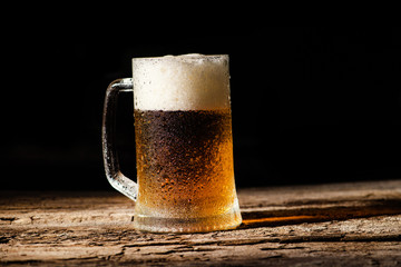 Beer. Cold Craft light Beer in a glass with water drops on the wooden table over the black background.