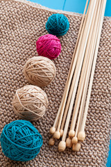 Fototapeta na wymiar Colorful balls and wooden needles lying on beige knitted background