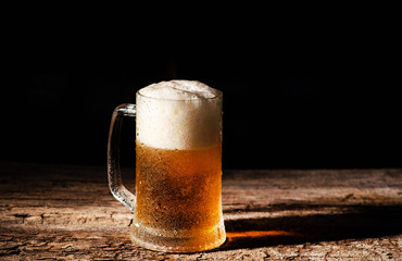 Beer. Cold Craft light Beer in a glass with water drops on the wooden table over the black background.