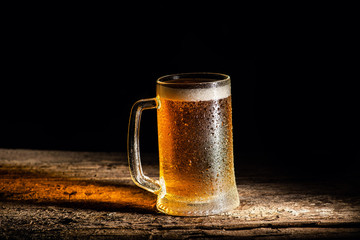 Beer. Cold Craft light Beer in a glass with water drops on the wooden table over the black background.