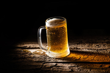 Beer. Cold Craft light Beer in a glass with water drops on the wooden table over the black background.