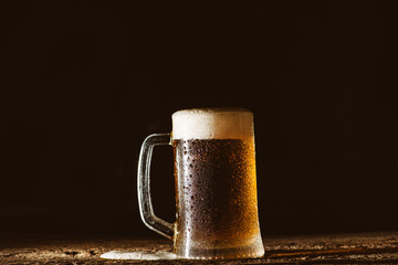 Beer. Cold Craft light Beer in a glass with water drops on the wooden table over the black background.