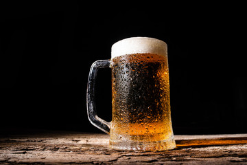 Beer. Cold Craft light Beer in a glass with water drops on the wooden table over the black background.