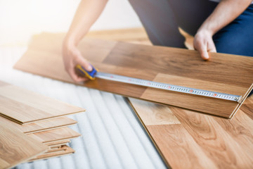 Worker hands installing timber laminate floor. Wooden floors house renovation with measure items.