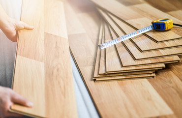 Worker hands holding timber laminate floor. Wooden floors house renovation with roll measure item.