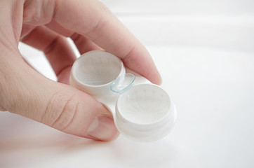 the girl is holding a container for soft contact lenses and a lens on her finger